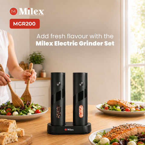 Milex MGR200 electric grinder set with two black cylindrical grinders on a matching base, shown on a wooden table in a kitchen setting with food dishes and a person partially visible in the background.