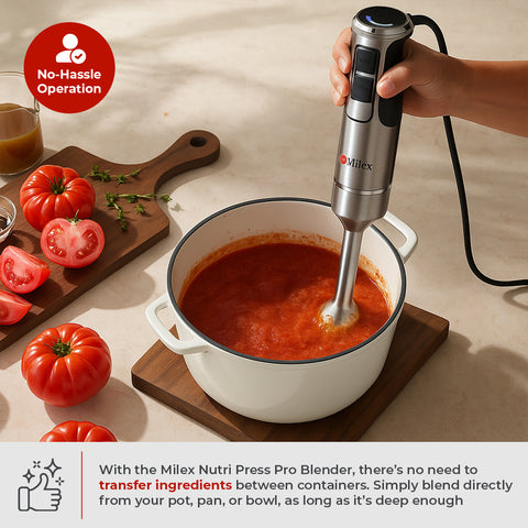 Milex Nutri Press Pro Blender being used to blend tomato soup in a pot on a table with tomatoes and a cutting board.