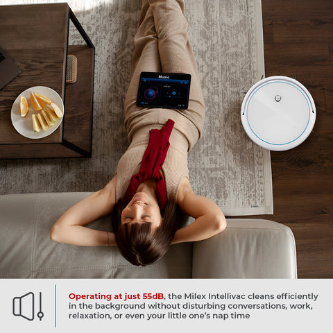 Woman lying on a couch with a smartphone, a plate of fruit, and a Intellivac 3-in-1 Robot Vacuum Cleaner in a living room.