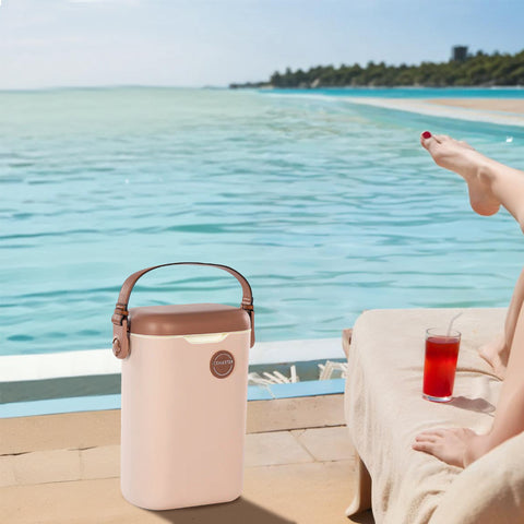 Beige portable cooler with brown handle by a poolside with a person sitting on a lounge chair.