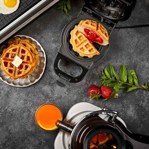 Waffle maker with waffles, strawberries, and a coffee pot on a dark surface