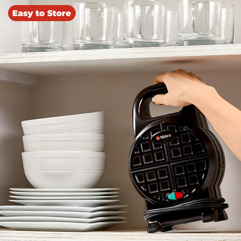 Black waffle maker held by a hand with stacked white dishes in the background